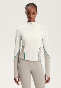 Jachetă sport albă cu accente teal, închidere cu fermoar și mâneci lungi. Prezintă un design ajustat și panouri bej contrastante pe lateral.