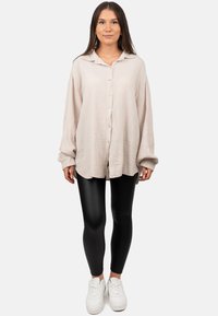 Licht beige overhemd met knopen van een gestructureerde stof en een losse pasvorm, gecombineerd met zwarte leggings en witte sneakers.