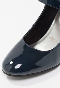 Chaussure Mary Jane en cuir verni bleu marine pour femmes, avec bout arrondi et semelle intérieure argentée coussinée, affichant les détails de face et de côté.