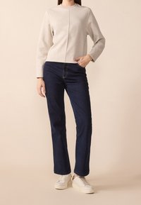 Sweat-shirt gris clair à manches longues et col rond, associé à un jean droit bleu foncé et des baskets blanches.