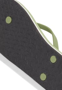 Grøn flip-flop sål med en tekstureret sort gummioverflade, der har cirkulære detaljer og en hvid kant. Designet til greb og komfort.