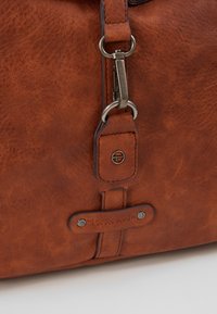 Borsa in pelle marrone con una finitura testurizzata, hardware in metallo e dettagli cuciti. Include un'etichetta di marca prominente e un attacco a clip.