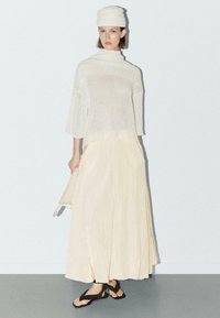 Dzianinowy kremowy top z krótkimi rękawami, nałożony na luźną, jasnop yellow spódnicę, zestawiony z czarnymi sandałami na paski. Miękkie tekstury i luźny krój.