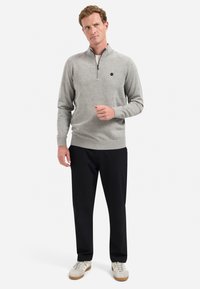 Hellgrau, zip-up Pullover aus Strickstoff mit langen Ärmeln und gerippten Bündchen. Kombiniert mit schwarzen Hosen und Sneakern.