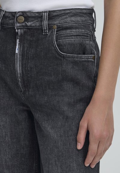 Tamsiai pilkos džinsinės kelnės su struktūrizuotu fasonu. Savybės: užsegimas mygtuku, priekinės kišenės ir išskirtiniai siuvinėjimo elementai.