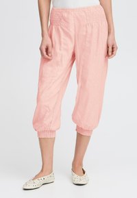 Pantalons capri légers de couleur rose clair avec une taille froncée et des poignets élastiques. Texture lisse et poches latérales visibles.