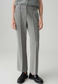 Persona che indossa pantaloni grigi su misura e scarpe stringate in pelle nera, in piedi davanti a uno sfondo neutro.