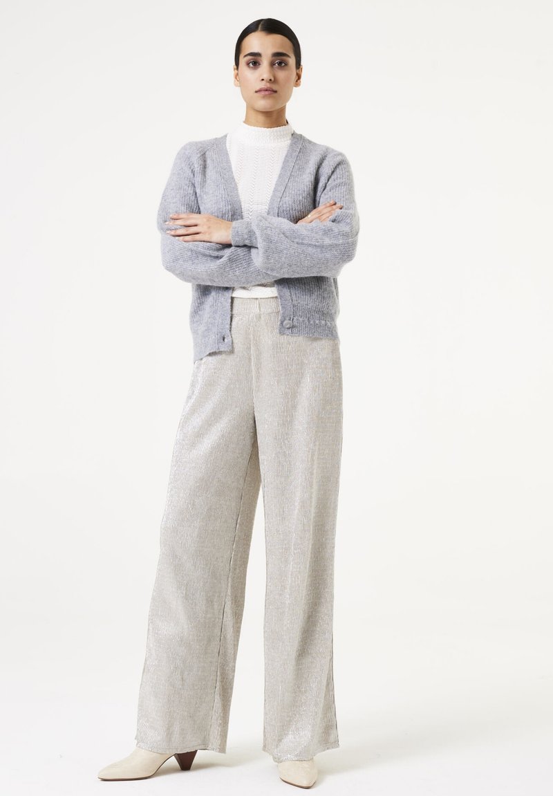 Lichtgrijze cardigan met een textuur oppervlak, gedragen over een witte geribbelde top, in combinatie met metalic wijde broekspijpen en crèmekleurige enkellaarsjes.