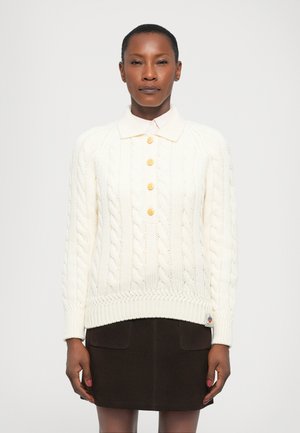 Cream cable-knit sweater with a collared neck, featuring four golden buttons and ribbed cuffs, paired with a dark brown skirt.