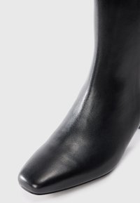 Stivale nero in pelle alla caviglia con texture liscia, punta affusolata e un tacco moderato, caratterizzato da un design elegante.