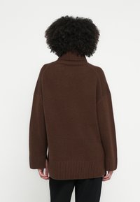 Pulover maro cu guler înalt, cu croială lejeră, tiv striat și mâneci largi. Confecționat din material tricotat texturat, ideal pentru stratificare.