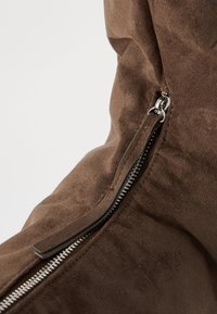 Bota de camurça castanha com um fecho lateral. Apresenta uma textura elegante e suave, e um fecho metálico para um encerramento seguro.