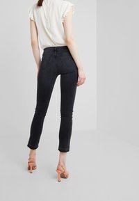 Jeans ajustados negros de talle alto, con bolsillos traseros detallados y dobladillo deshilachado. Combinados con sandalias de tacón alto en rosa claro.