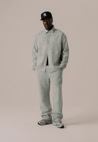 Szary, teksturowany zestaw z marynarką i spodniami, zawierający marynarkę na guziki oraz spodnie o luźnym kroju, do tego czapka z daszkiem w kolorze czarnym i szare tenisówki.