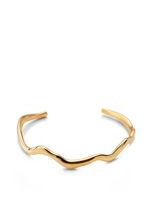 Kultasävyinen avoin kalterirannekoru, jossa sileä, epäsäännöllinen aaltoileva muotoilu ja kiillotettu pinta valkoisella taustalla.