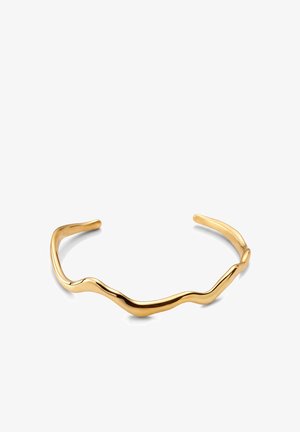 Armbånd i guldton med åben manchet, glat og uregelmæssigt bølget design og poleret finish på hvid baggrund.