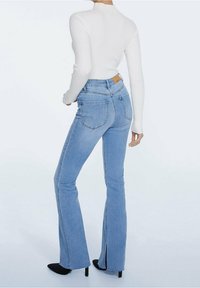 Lichtblauwe flared jeans met een hoge taille, met een gestructureerde weving, meerdere achterzakken en een kleine split aan de zoom. Gepaard met een witte geribde top.