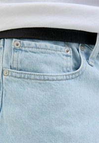 Jeans de denim azul claro con un bolsillo delantero visible, remaches plateados y un cinturón negro texturizado en la cintura. Textura suave y lisa.