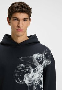 Felpa nera con cappuccio realizzata in morbido cotone, con un design grafico bianco sulla parte anteriore. Comprende un cappuccio con cordoncino e una vestibilità rilassata.