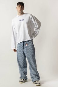 Hvit langermet skjorte med blå tekst, kombinert med blå rutete, vide jeans med rød brodert design, og hvite joggesko.