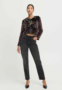 Sort, paljetteret cropped jakke med store sorte bånddetaljer, parret med højtaljede sorte jeans og spidse sorte sko.