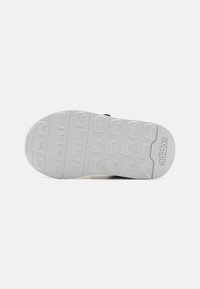 Suela de zapatilla blanca con patrón texturizado y estrías, con detalles de logo grabado, hecha de goma para proporcionar tracción y durabilidad.