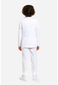 Completo bianco con giacca su misura e pantaloni dritti. Tessuto liscio, cuciture minime e sneaker bianche per un look pulito.