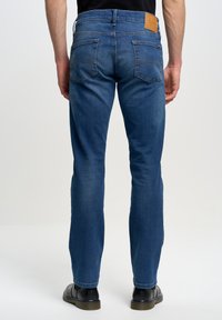 Jeans de mezclilla azul oscuro con un diseño de corte recto, que cuentan con dos bolsillos traseros y un parche de cuero en la cinturilla. Textura suave.