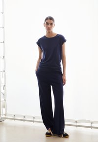 Navyblauw T-shirt met opgerolde korte mouwen, gecombineerd met wijde navybroek. De outfit heeft een ontspannen pasvorm en een gladde stoftextuur.