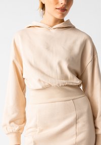 Beige Kapuzenpullover aus weichem Stoff mit lockerer Passform und geripptem Saum. Verfügt über eine gefütterte Kapuze und überschnittene Schultern für zusätzlichen Komfort.