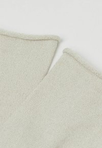 Beige glitrende sokker med ribbet tekstur, der har en foldet manchet ved hver topkant. Subtil glans i materialet.
