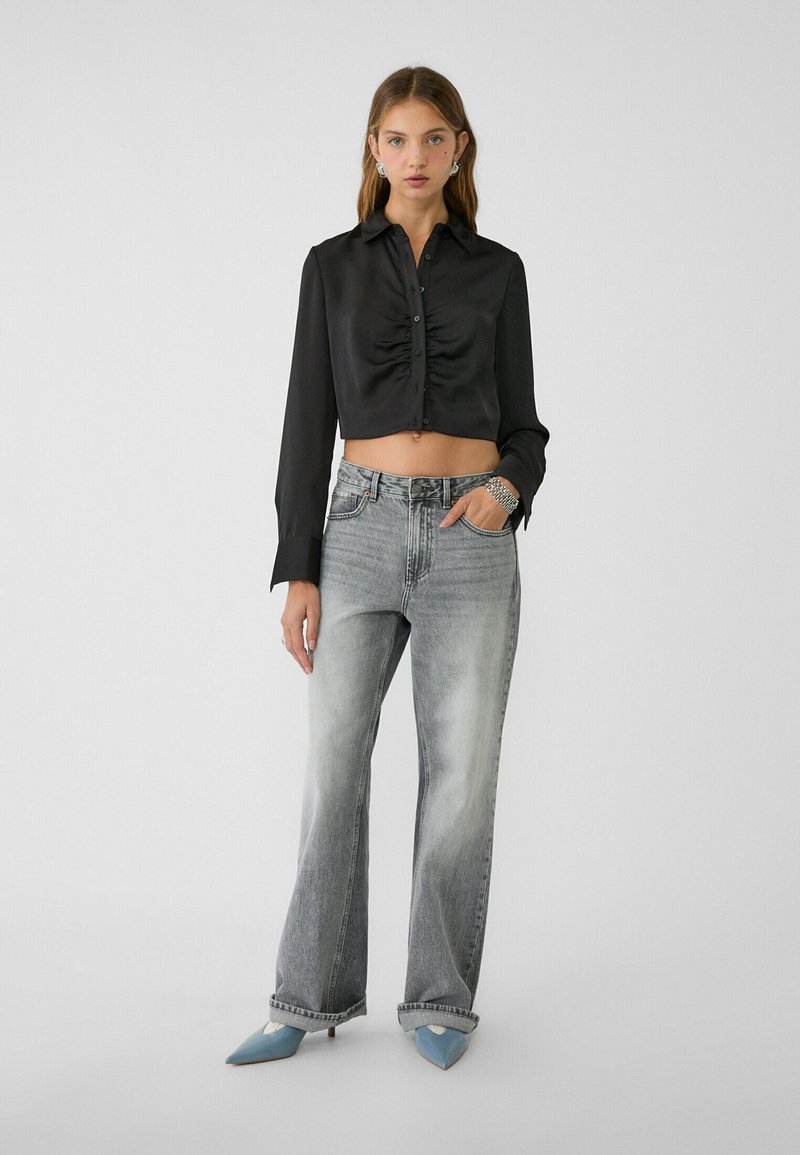 Chemise noire en satin cropped avec fronces à l'avant, associée à un jean large gris délavé taille haute et des escarpins pointus bleu clair.