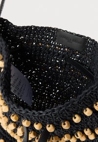 Juoda megzta rankinė su mediniais karoliukais aplink kraštą, odine raišteliu ir vidine etikete su užrašu „Vanessa Bruno Paris“.