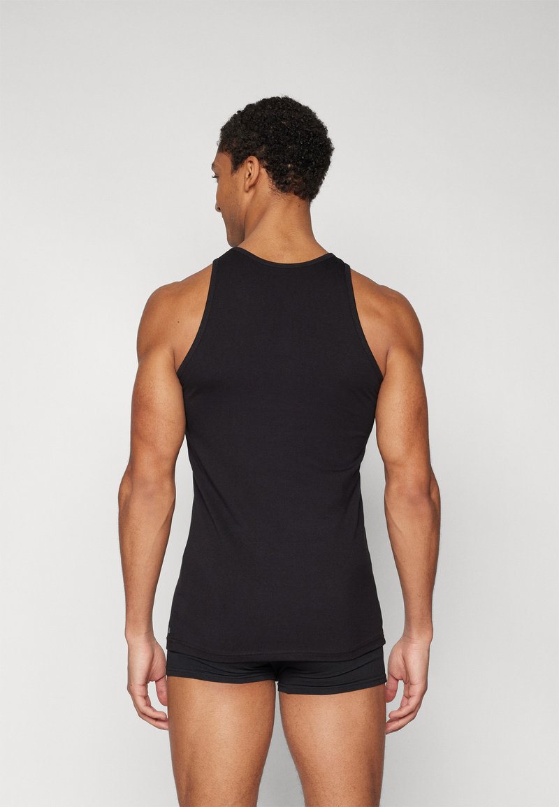 Czarna koszulka na ramionkach wykonana z bawełny, z okrągłym dekoltem i dopasowanym krojem. Noszona z czarnymi szortami.