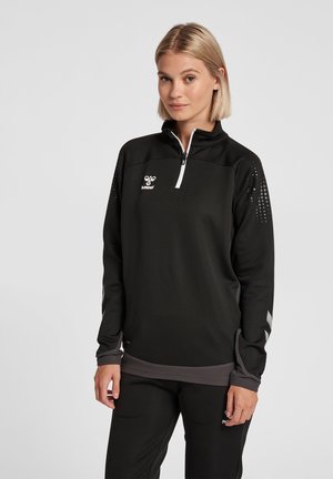 Zwarte half-rits sporttop van een gestructureerde stof, met een zilveren rits en een stippenpatroon op de schouders. Bevat een logo op de borst.