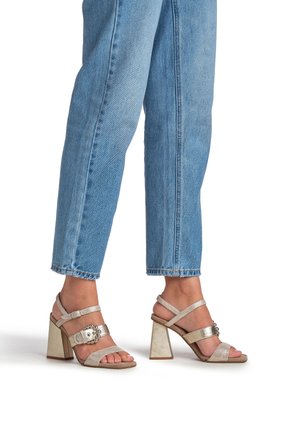 Block-heeled sandals in beige with textured straps and a decorative silver buckle; paired with light blue cropped jeans.