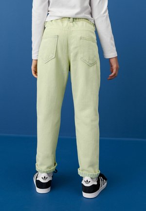 Hellgrüne Jeanshose mit entspannter Passform, zwei Gesäßtaschen und hochgekrempelten Säumen, kombiniert mit schwarz-weißen Turnschuhen auf einem blauen Hintergrund.