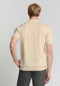 Beige polo shirt met korte mouwen van een zachte textuur, met een geribbelde kraag en zoom. De stof heeft een subtiel melangepatroon.