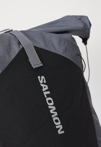 Mochila cinza e preta com um exterior durável, design elegante, fecho ajustável e o proeminente logo "SALOMON" em prata.