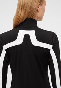 Svart bodysuit med hög krage har vita paneldetaljer, strömlinjeformad design och en slät textur som framhäver en modern silhuett.