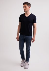 Námořnické tričko s krátkým rukávem a výstřihem do V v kombinaci s tmavě modrými slim-fit džíny a bílými teniskami. Jednoduchý design s hladkým povrchem.