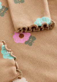 Brunt ribbet stof med pastelfarvede blomsterprint med aqua- og lyserøde blomster. Kanterne har en flæsekant for ekstra tekstur.