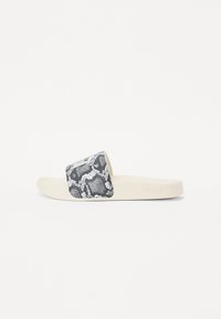 Sorte og hvite slangeskinnmønster sandal med en myk, beige gummi såle. Har en bred stropp og merket logo på siden.