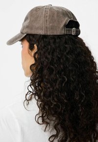 Cappello marrone, usurato, realizzato in tessuto con visiera curva. Presenta una cintura regolabile sul retro e dettagli di cucitura visibili.