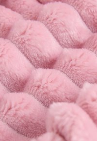 Tissu en peluche rose avec une surface texturée ondulée présentant des bouffées douces et surélevées. Le matériau semble duveteux et accueillant.