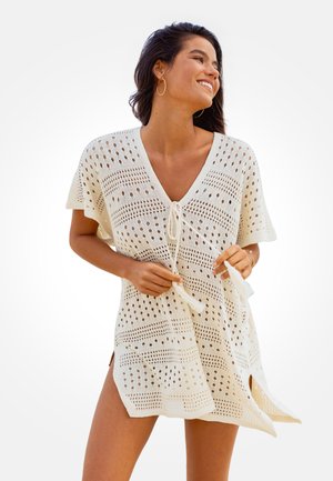 Witte gehaakte cover-up met een V-hals, korte mouwen en verstelbaar koord aan de voorkant. Heeft open patronen en zijsplitten voor extra ventilatie.