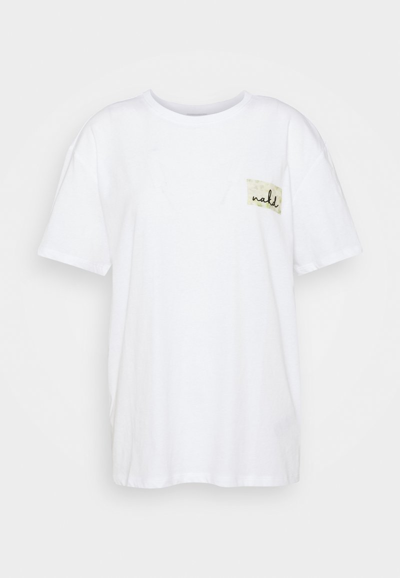 T-shirt blanc à manches courtes avec col rond, avec un petit patch rectangulaire beige et un texte en cursive noire sur la partie gauche de la poitrine.