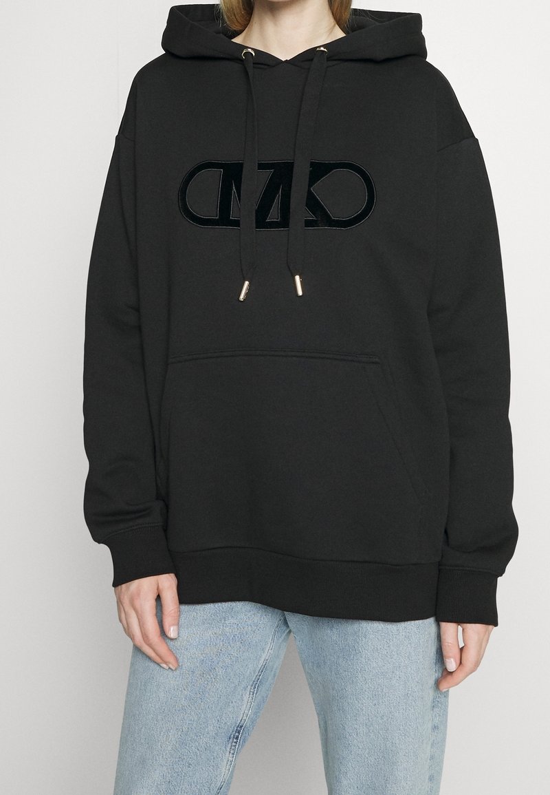 Felpa nera con cappuccio, caratterizzata da un logo in peluche, cordini con punte dorate e una tasca a marsupio frontale. Tessuto morbido con una vestibilità comoda.