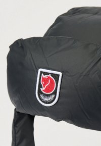 Černá prošívaná bunda s obdélníkovou nášivkou zobrazující červenou liščí hlavu a bílé kapradinové listy na černém pozadí v oblasti ramene.