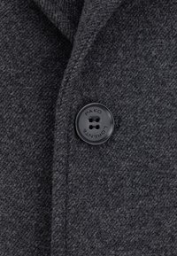 Szary wełniany płaszcz z czarnym guzikiem z czterema otworami, wytłoczonym napisem "PAKO LORENTE". Tkanina ma teksturowany, tkany wygląd.